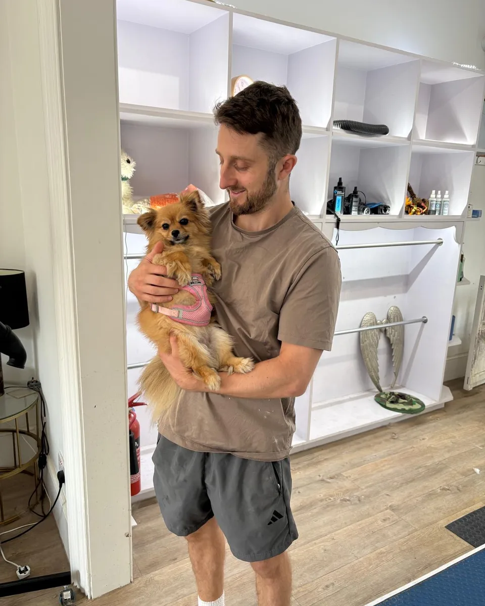 Oli, owner of Canine Beauty, holding a fluffy Pomeranian in the salon